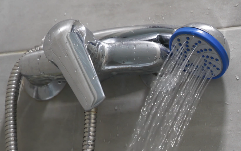 Close-up of a handheld showerhead spraying water from a chrome bathroom fixture.