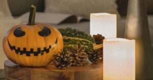 Jack-o’-lantern displayed on a wooden table alongside pinecones, decorative gourds and glowing flameless candles, creating a warm autumn Halloween centerpiece.